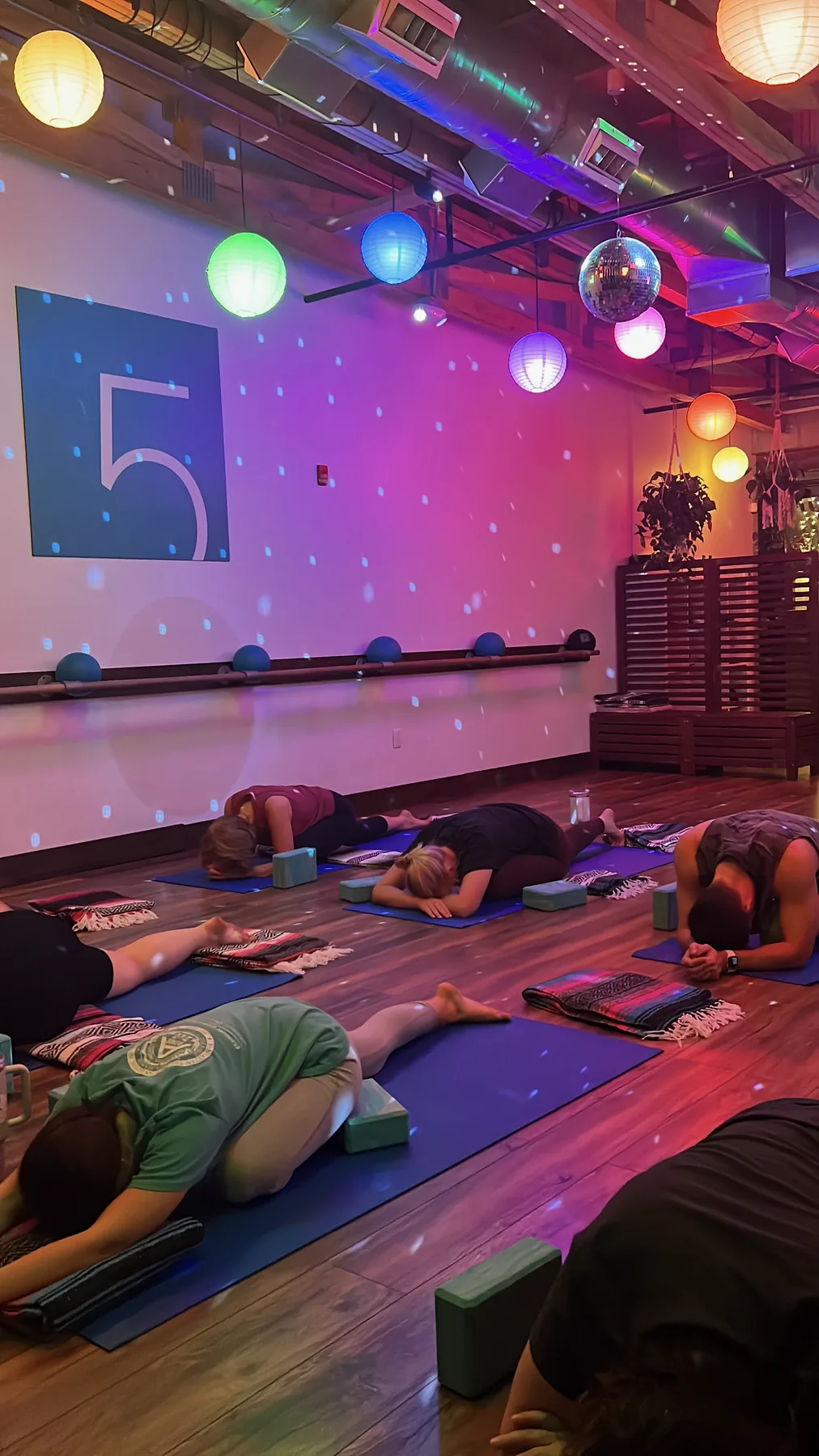 A class mid-session at TenPoint5 — members lying on mats stretching under disco-ball and paper-lantern lighting, with the studio's '5' wall mark visible