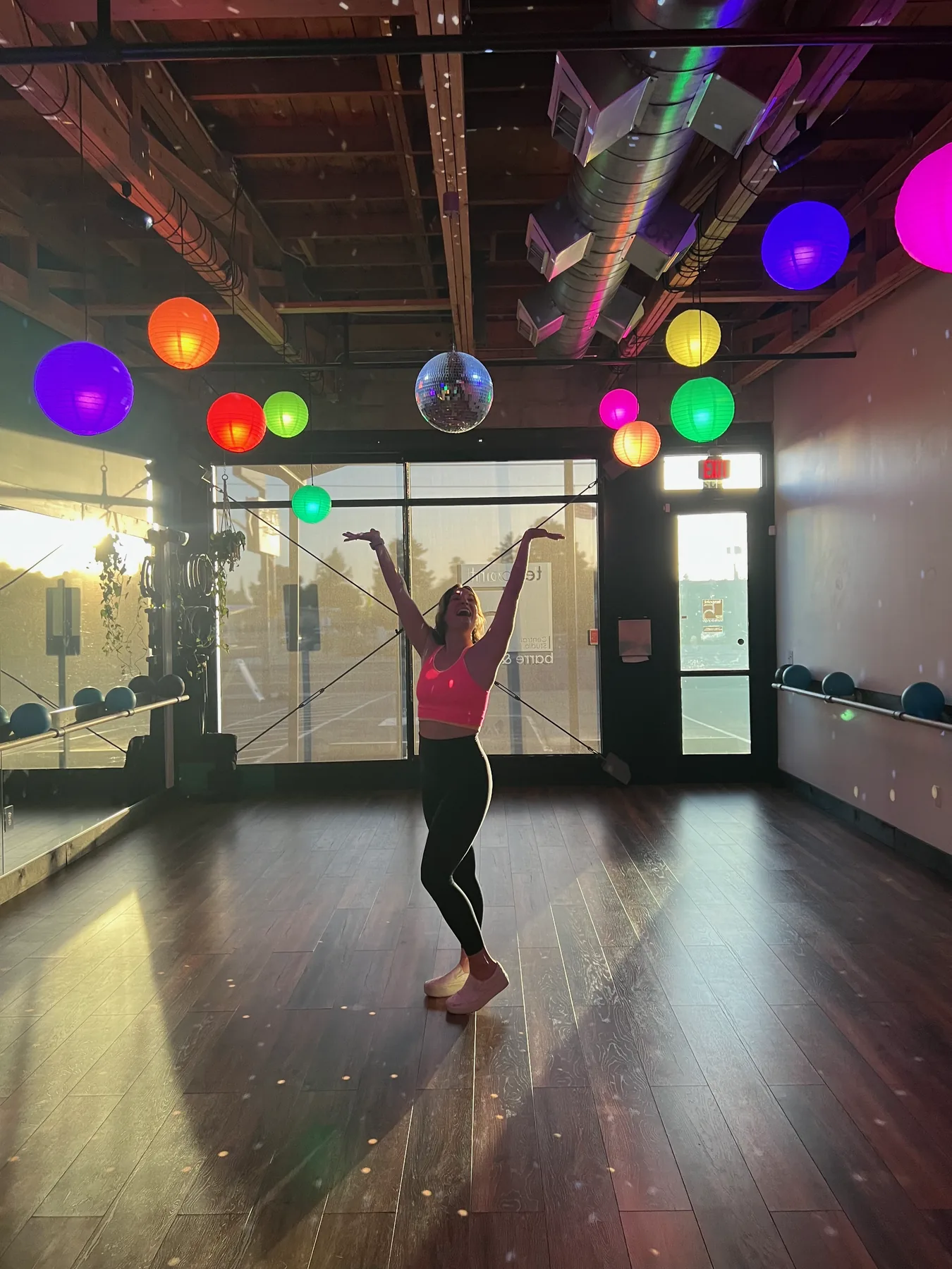 A single member with arms raised mid-pose in the TenPoint5 studio under a row of colored paper lanterns and a disco ball
